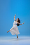 Young and incredibly beautiful ballerina is posing and dancing at blue studio full of light.