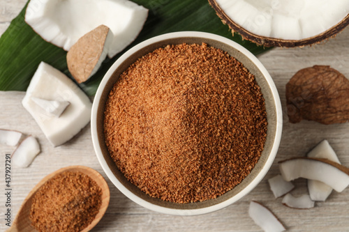 Natural coconut sugar in bowl on white wooden table, flat lay