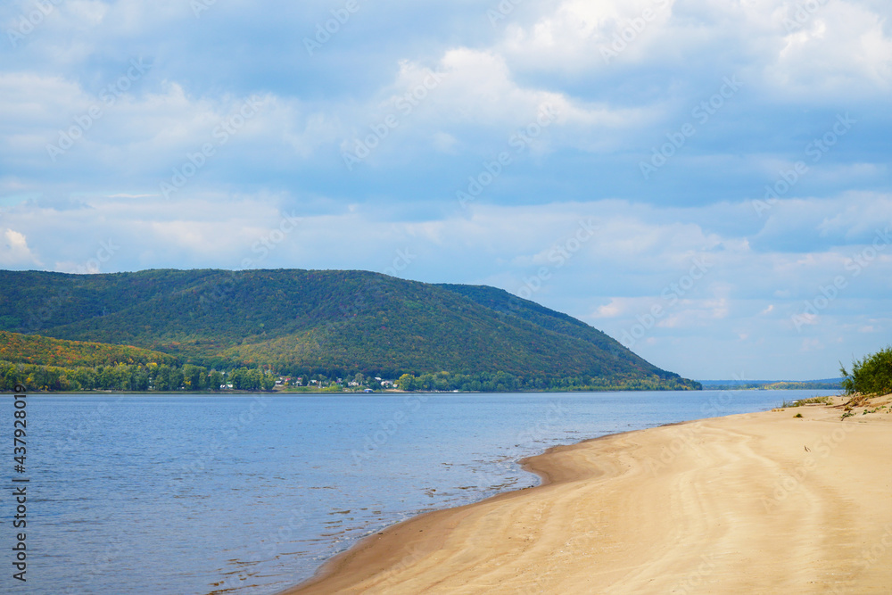 The sandy shore of the big Volga river against the background of a cloudy sky. On the opposite bank of the Zhiguli Mountains