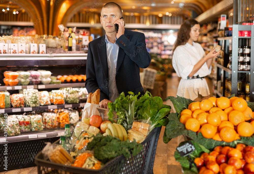 Young focused man using phone during shopping at supermarket