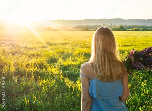 Beautiful girl holding bouquet of summer flowers of purple lupins. Young happy woman enjoying nature. Hello summer. Wellness, harmony and freedom