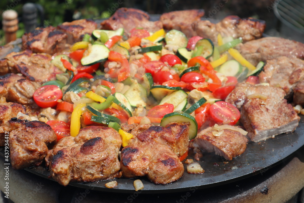 Grilling in a cast iron pan. Meat - pork neck with vegetables: onion, mushrooms, colorful peppers and zucchini
