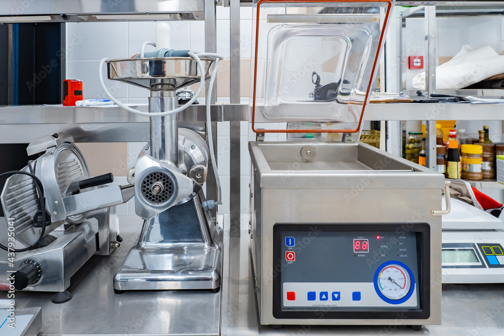 Professional cook equipment. Vacuum sealer next to the meat grinder. Concept - equipment for restaurants. Professional restaurant equipment. Devices for cooking and packaging food. Slicer Professional cook equipment. Vacuum sealer next to the meat grinder. Concept - equipment for restaurants. Professional restaurant equipment. Devices for cooking and packaging food. Slicer