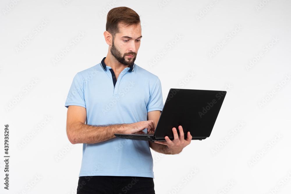 Man with laptop on a light background. Man works with laptop while standing. Portrait of young guy with laptop computer. Concept - sale of laptops. Computer hardware store. Guy is typing something