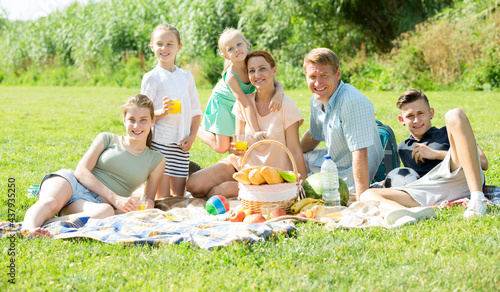 Positive parents with four kids in different age having picnic outdoors on sunny day