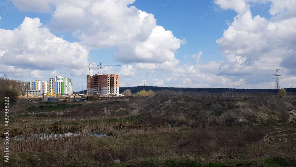 A snapshot of the field and the construction of multi-apartment high-rise residential buildings that began there on a sunny day. Construction work of a new residential area. A snapshot of the field and the construction of multi-apartment high-rise residential buildings that began there on a sunny day. Construction work of a new residential area.