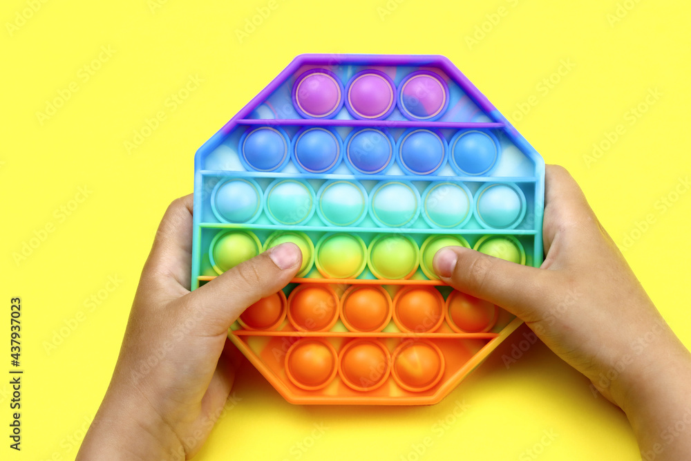 kid hands playing with colorful rainbow pop It on yellow background kid hands playing with colorful rainbow pop It on yellow background