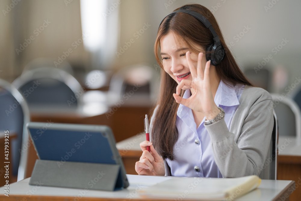Young interactive happy Asian teenage girl university student studying and presenting her lesson online via video call on a digital tablet in the classroom alone herself. Education stock photo Young interactive happy Asian teenage girl university student studying and presenting her lesson online via video call on a digital tablet in the classroom alone herself. Education stock photo