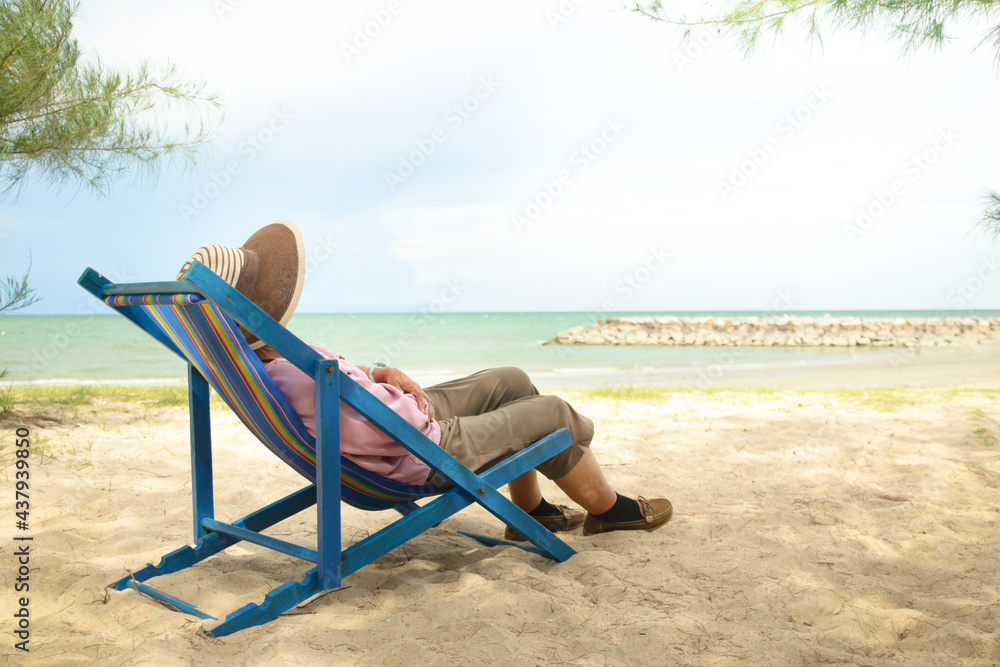 Asian old woman wearing a sun hat Lie down on a deck chair by the beach. Concept of natural tourism of the elderly during retirement age. Copy Space