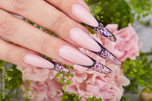 Hand with long artificial purple french manicured nails decorated with rhinestones and pink rose flowers. Fashion and stylish manicure.