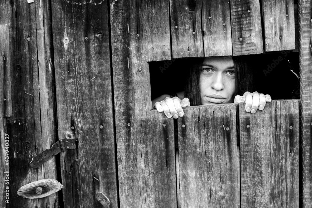 An woman looking through the crack of a locked wooden shed. Black and white photo. An woman looking through the crack of a locked wooden shed. Black and white photo.