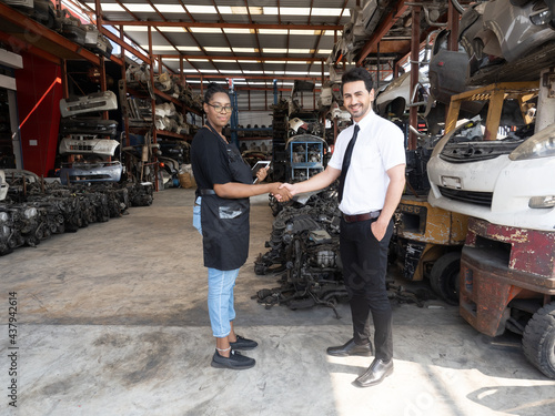 African woman salesperson shaking hands with Caucasian man customer after a successful deal at the automotive warehouse. .