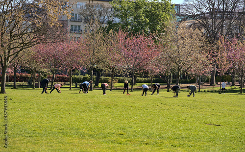 Beautiful morning distant view of big group of adult people attending yoga class, practicing social distancing and exercising yoga outside on lawn on sunny day in Herbert Park, Dublin, Ireland © Romio Shots