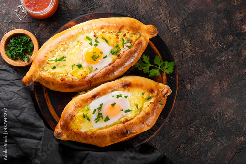  A traditional dish of Georgian cuisine, Adjarian khachapuri with cheese and egg and spicy tomato sauce adjika on the dark background top view, free space for text