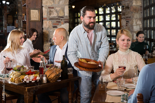 Young hospitable owner of rustic restaurant serving traditional meals to guests..