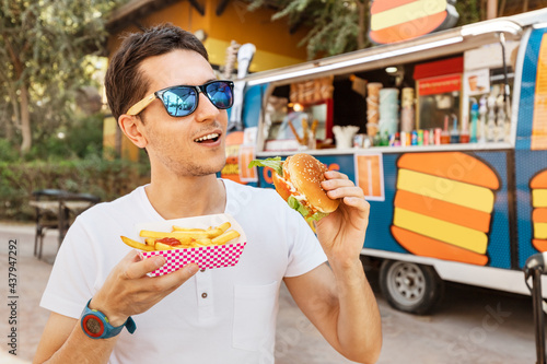 Happy man eats a burger and french fries near an outdoor food truck cafe. Streetfood and junk food concept photo