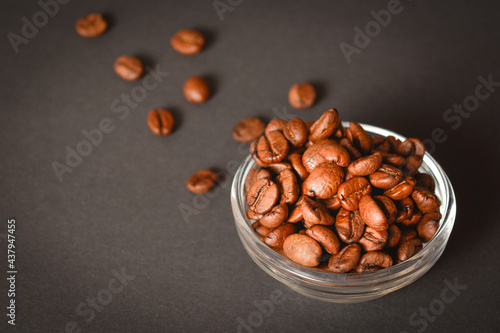 Side view of Roasted coffee beans in bowl with scattered seeds on dark background. High quality organic aroma seeds. Copy space text image  © Art Food