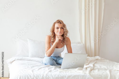 Enjoying time at home. Beautiful young smiling woman working on laptop while sitting in a comfortable bed at home