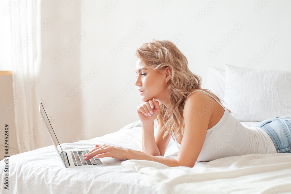Happy casual beautiful woman working on a laptop sitting on the bed at home Happy casual beautiful woman working on a laptop sitting on the bed at home