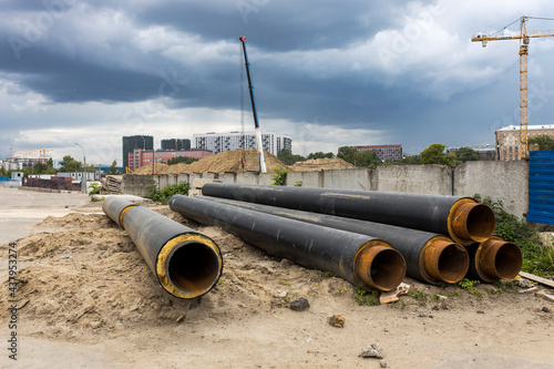 Long factory pipes lie on the ground against the backdrop of a residential area under construction