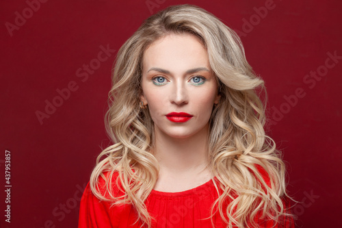 Perfect woman fashion model with healthy blonde curly hair styling and makeup on red background