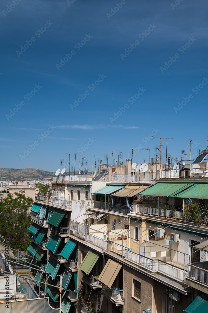 Fototapeta premium Cityscape of Athens, Greece. Typical urban architecture. Exterior of living buildings. Sun blinds on the terraces. Sunny summer day. Green trees. Roof-mounted antennas.