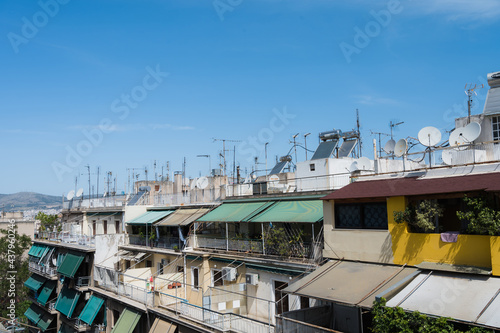 Cityscape of Athens, Greece. Typical urban architecture. Exterior of living buildings. Sun blinds on the terraces. Sunny summer day. Green trees. Roof-mounted antennas.