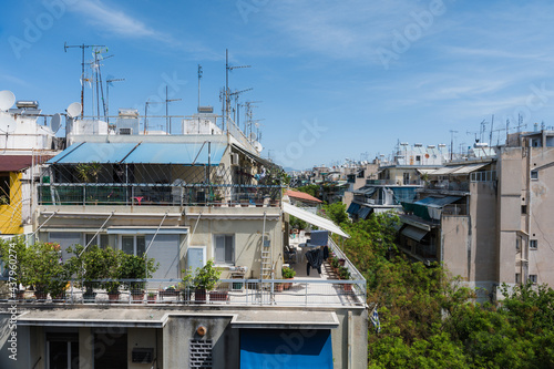 Cityscape of Athens, Greece. Typical urban architecture. Exterior of living buildings. Sun blinds on the terraces. Sunny summer day. Green trees. Roof-mounted antennas.