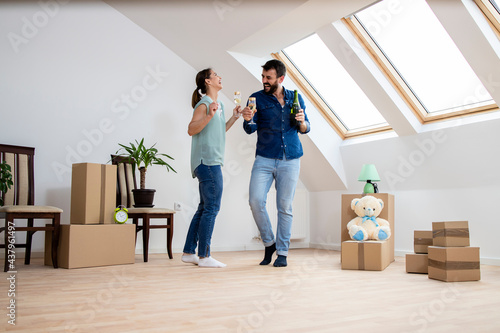 House moving concept - young caucasian couple dancing and drinking champagne to celebrate their very first day in new home.