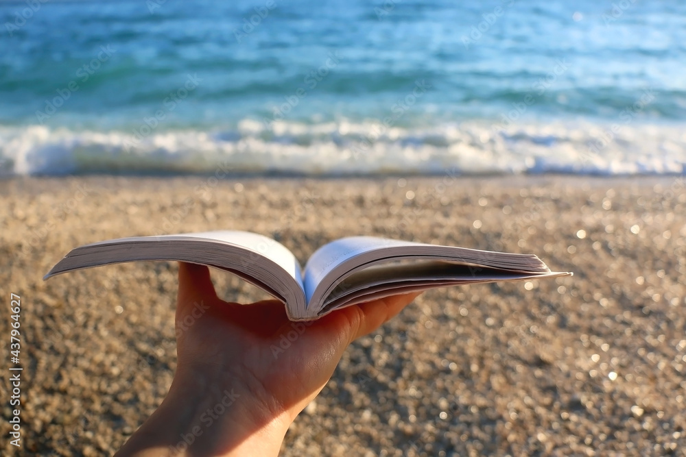 Hand holding open book on a beach. Selective focus. Hand holding open book on a beach. Selective focus.