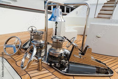 The bow of the yacht with teak deck, with anchor stops, part of the anchor chain, winch for tightening and ship bell made of stainless steel.