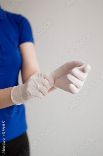 A young woman puts a white latex disposable medical glove on a hand on the white backgrounds.