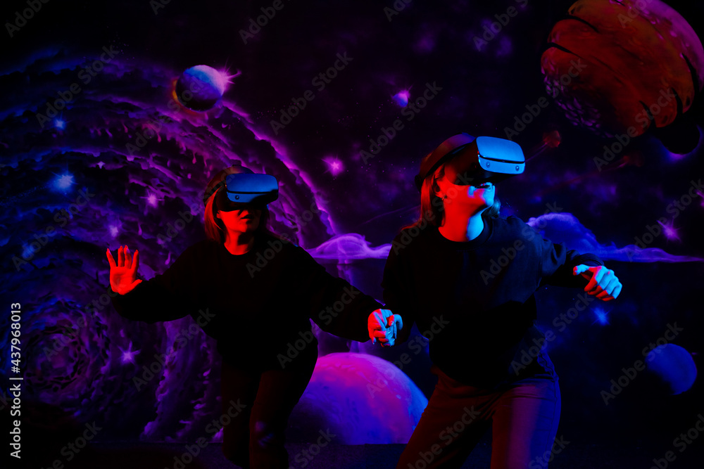 Two girls friends in virtual glasses are holding hands in the playroom in neon light