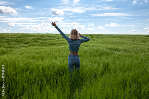 Woman on her back with outstretched arms. Slim young woman in the middle of a wheat field. Bright field of green grass. Blue sky with clouds.