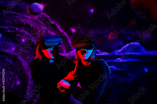 Two girls sisters friend with virtual glasses holding hands are having fun in the game room in neon blue and red light