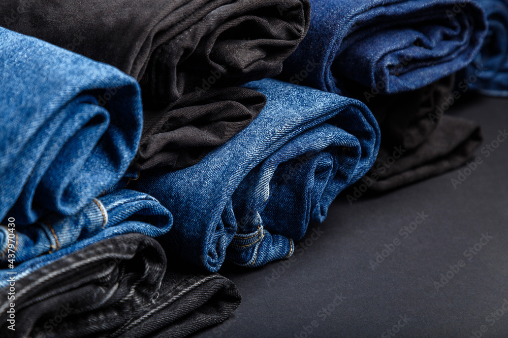 Blue jeans folded in rolls lie on black background. Black and blue denim  pants in form of rolls. Jeans trousers stack of casual wear. Clothes store  shop Jean textile for selling. Photos