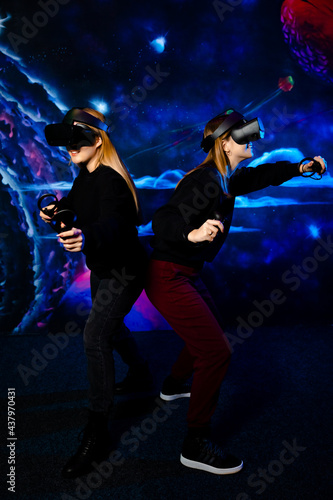 Two young girls sisters friend with virtual glasses have fun together and play video games