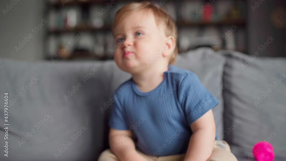 Cute baby boy lying down on sofa while stacking colorful plastic cups and sitting up back. Adorable toddler playing educational toy at home
