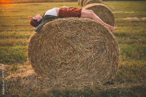 Φωτογραφία Beautiful carefree woman in hat lying on haystack in sunset light enjoying evening in summer field