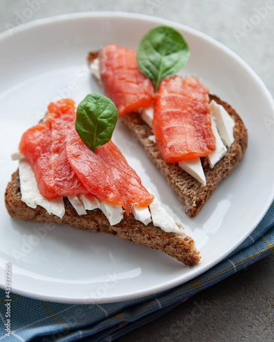 Bruschetta with red fish and cream cheese with black bread on white plate.