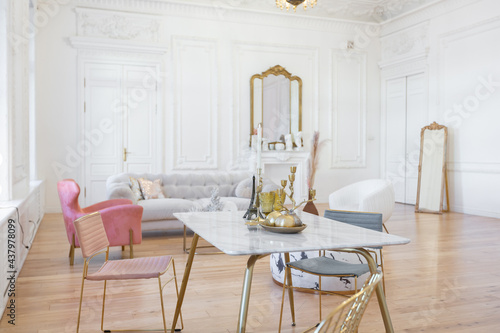 very light baroque style luxury interior of big sitting room. White walls decorated with awesome stucco. Royal style apartment with chic furniture with gold elements