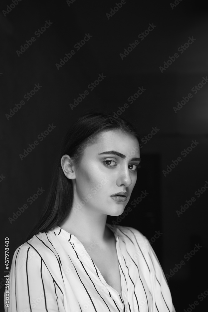 Black and white indoor portrait of a sad pretty young woman wears striped white shirt