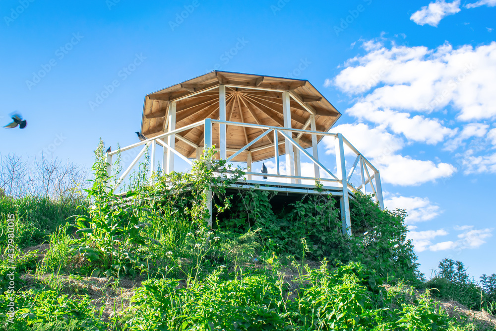 Beautiful wooden carved open alcove, arbor in city botanic park in spring summer sunny day against blue sky with bright sunlight Beautiful wooden carved open alcove, arbor in city botanic park in spring summer sunny day against blue sky with bright sunlight
