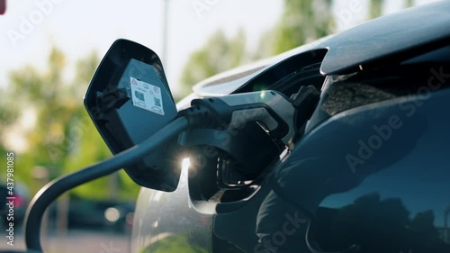 Man plugging in charger into an electric car at charge station. Slow motion