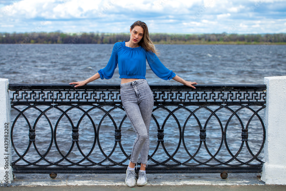 Portrait of a young brunette woman in a beige blouse with long sleeves and blue jeans