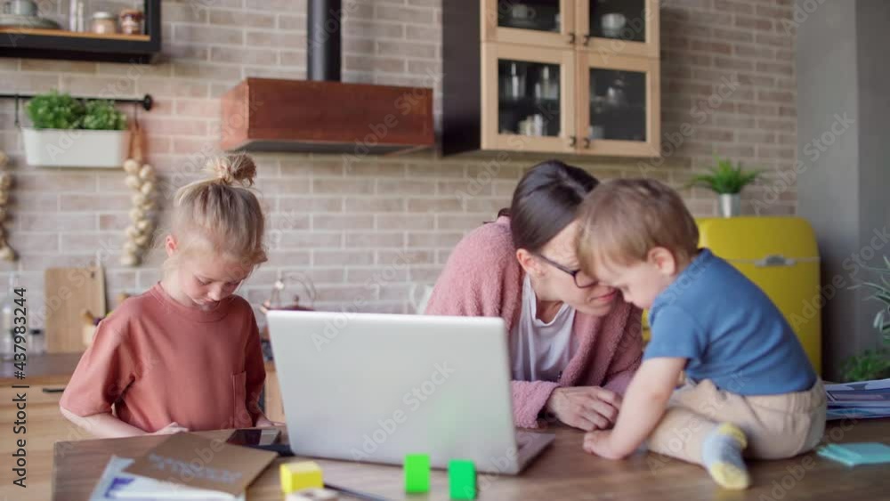 Mother of two working on laptop computer, playing with baby son and talking to little daughter. Busy woman working from home and caring of children Mother of two working on laptop computer, playing with baby son and talking to little daughter. Busy woman working from home and caring of children