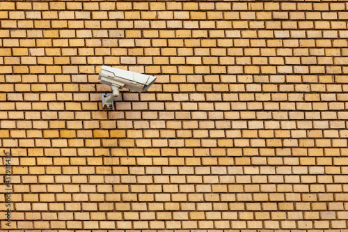 Surveillance camera attached to a yellow brick wall