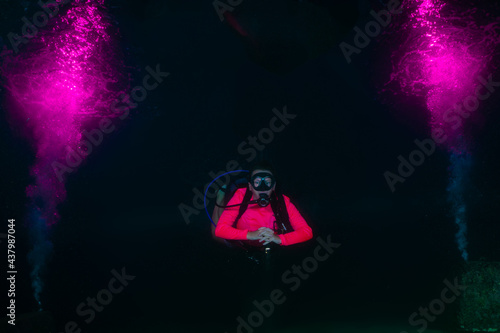A female scuba diver relaxes into a night dive as explosions of pink bubbles decorate the water around her