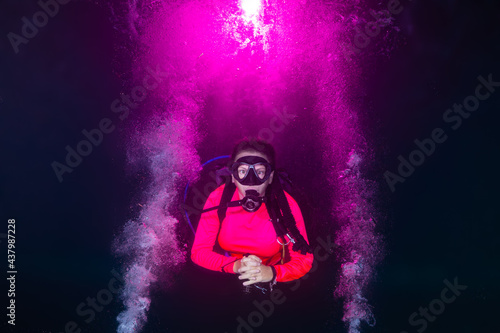 A female scuba diver relaxes into a night dive as explosions of pink bubbles decorate the water around her