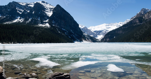 Beautiful view of Lake Louise melting at springtime. Frost on the surface of the lake, snowed mountains. Sunny day with blue sky. Banff National Park, Alberta, Canada